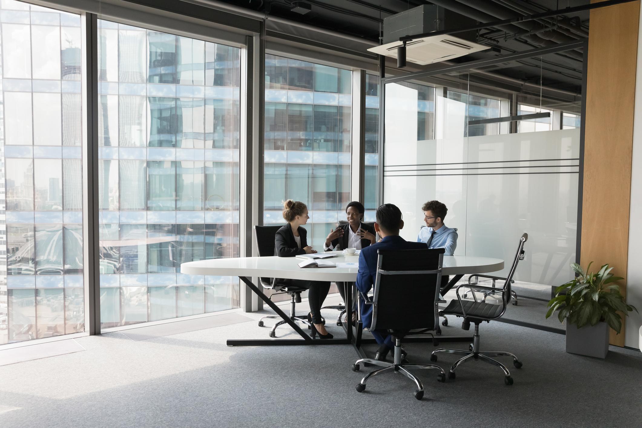 Team of 4 people sitting at a conference table in a big room