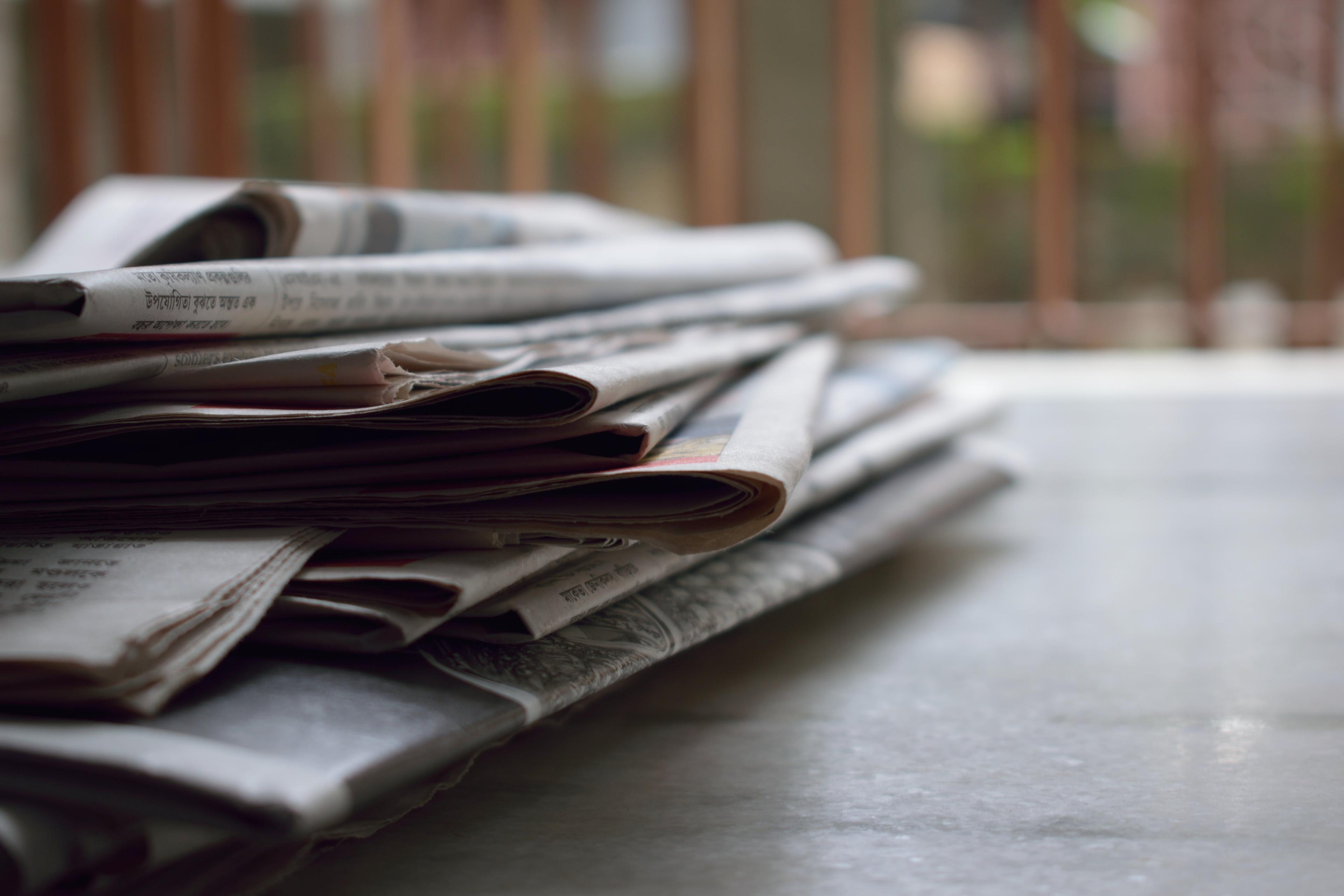 stack of magazines and newspapers sitting on a desk.