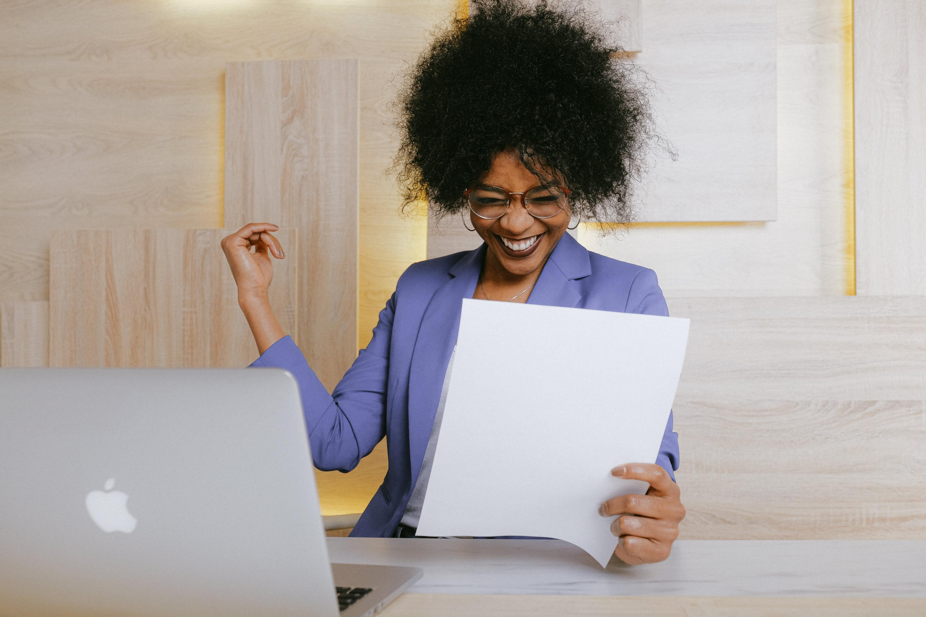 A black woman is holding a paper and smiling.