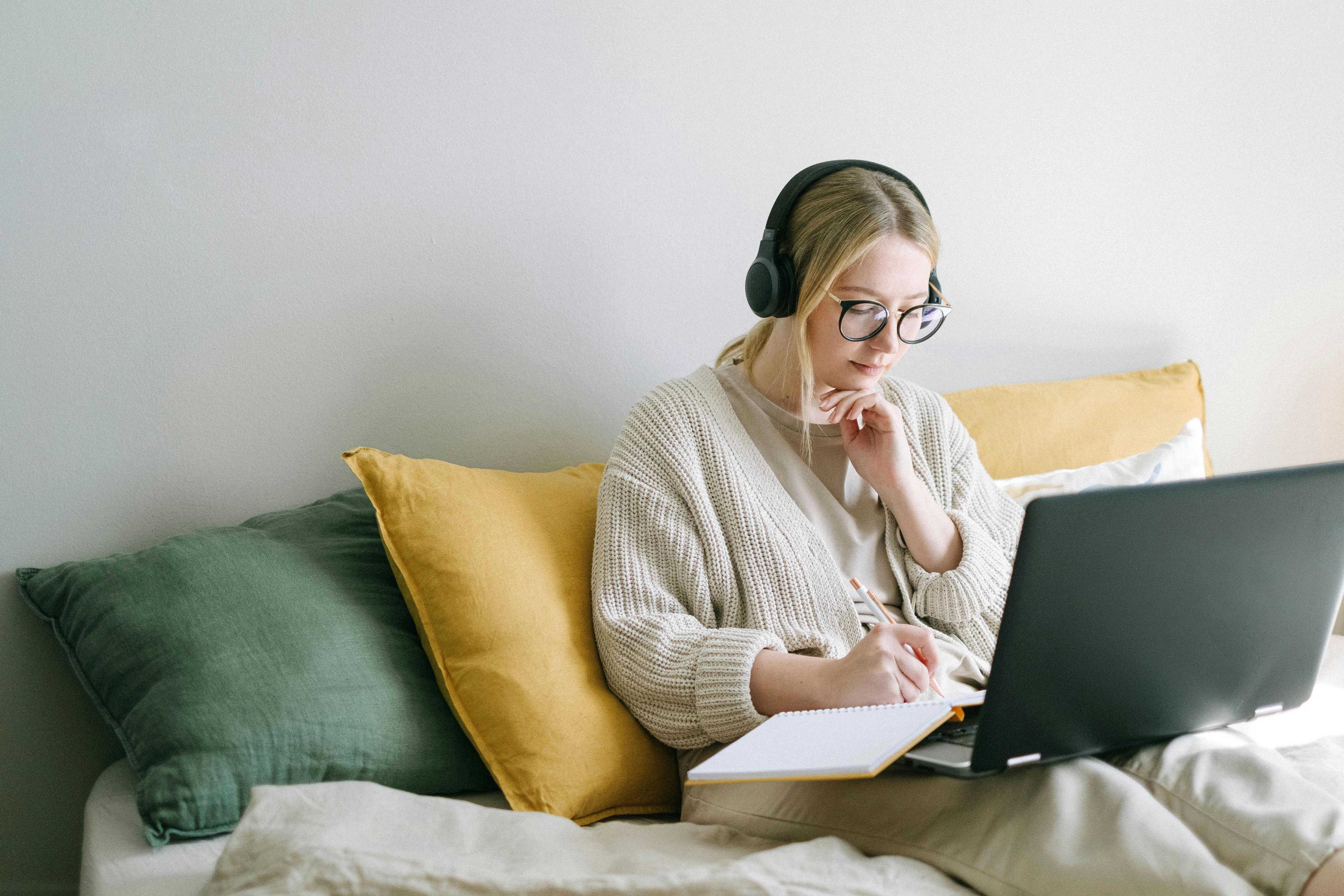 person sitting on couch looking at computer and writing on a notebook