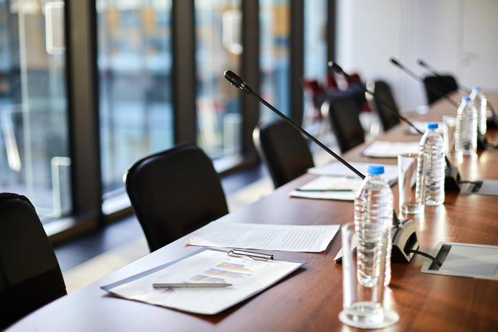 desk set up for panel at a conference with mics, packets of paper and water bottles for speakers